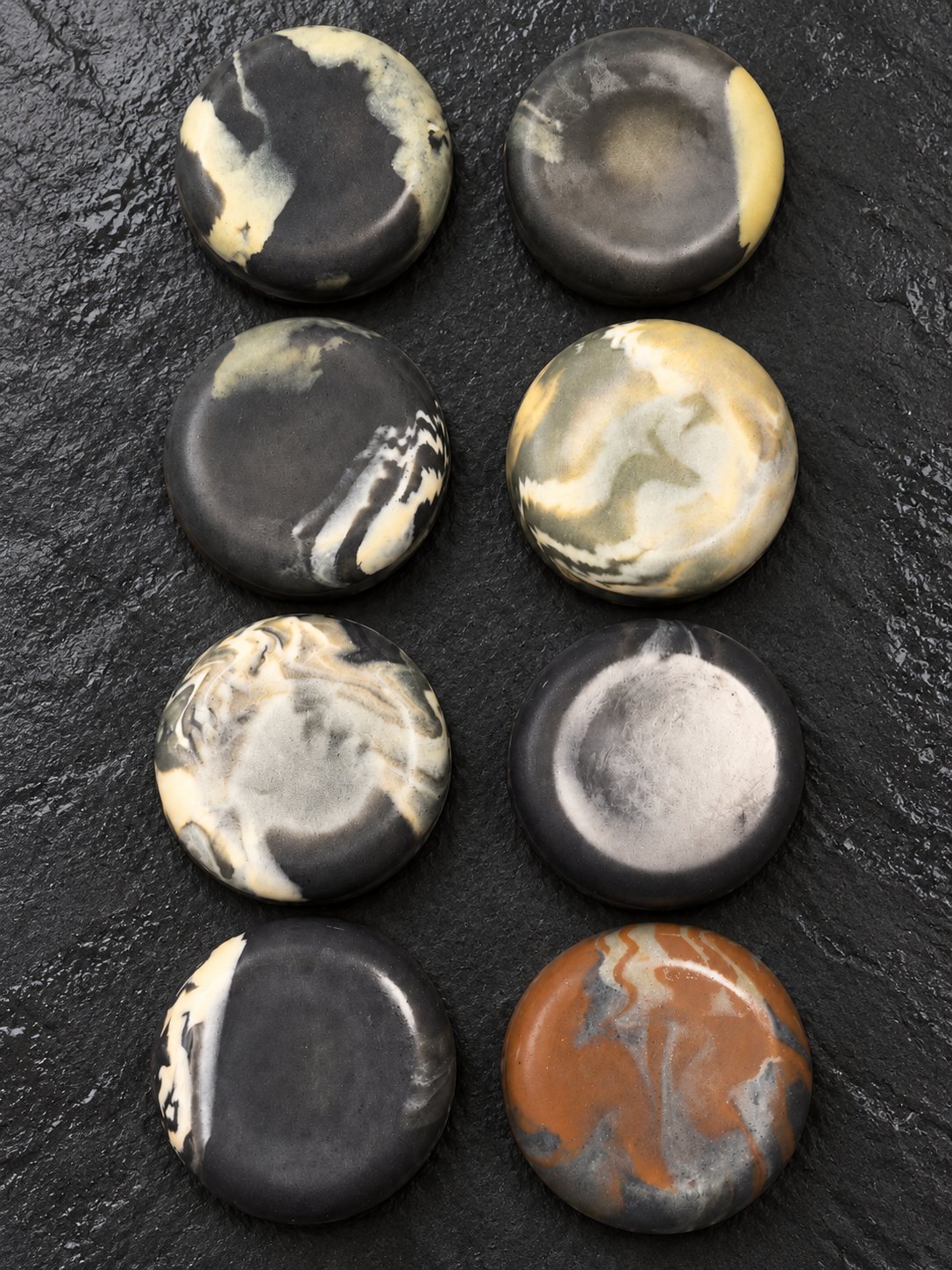 Blackwater river-stone soaps in charcoal, black and cream with one rust stone, on wet slate